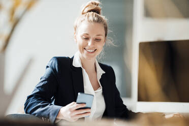 Smiling businesswoman using smart phone at office - JOSEF08998