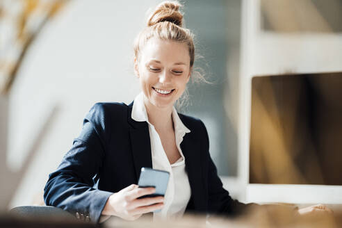 Lächelnde Geschäftsfrau mit Smartphone im Büro - JOSEF08998