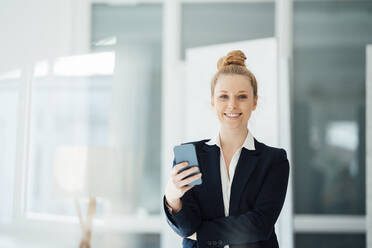 Geschäftsfrau mit Haarknoten hält Smartphone im Büro - JOSEF09007