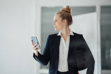 Businesswoman with helmet holding smart phone at office - JOSEF09008