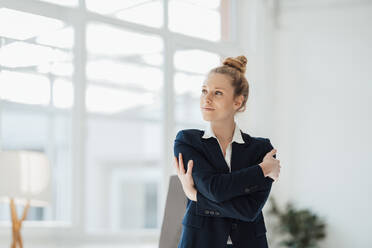 Contemplating businesswoman hugging self at office - JOSEF09012