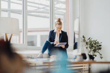 Businesswoman using tablet PC sitting near window at office - JOSEF09017