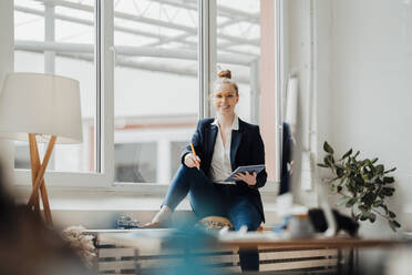 Young businesswoman with tablet PC sitting near window at office - JOSEF09018