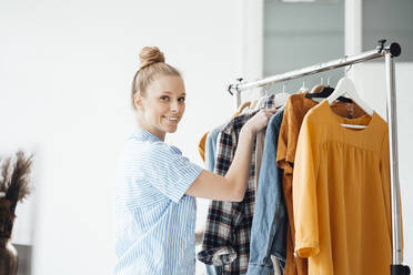 Smiling fashion designer arranging clothes in rack at studio - JOSEF09034