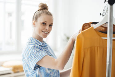 Junge Modedesignerin in der Nähe des Kleiderständers im Atelier - JOSEF09035