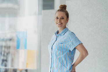 Smiling fashion designer with hair bun standing in studio - JOSEF09049