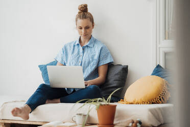 Working woman using laptop sitting on bed at home - JOSEF09054