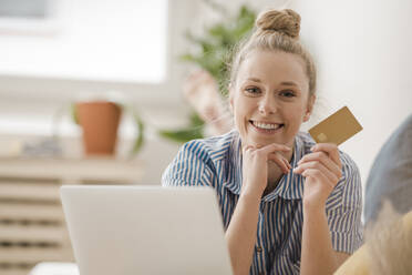 Lächelnde Geschäftsfrau mit Hand am Kinn, die ihre Kreditkarte zu Hause vorzeigt - JOSEF09062