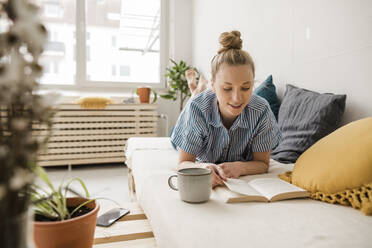 Businesswoman reading book lying down on bed at home - JOSEF09065