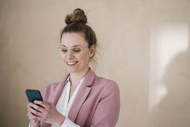 Geschäftsfrau mit Brille und Smartphone an der Wand - JOSEF09102