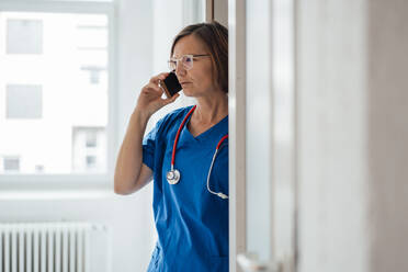 Arzt, der mit seinem Smartphone in der Tür einer Klinik steht - JOSEF09112