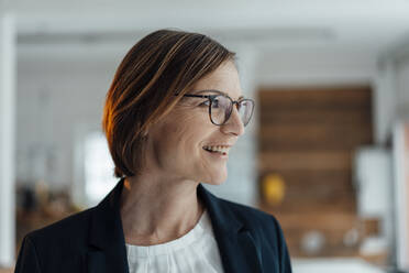 Smiling businesswoman wearing eyeglasses in office - JOSEF09114