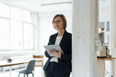 Businesswoman with tablet PC leaning on column in office - JOSEF09123