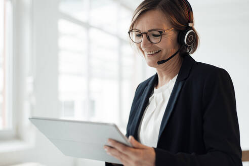 Happy telecaller wearing headset using tablet PC in office - JOSEF09128