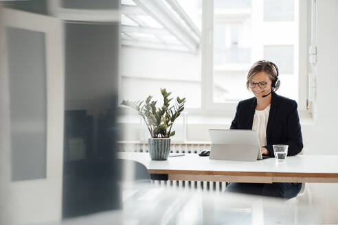 Happy businesswoman wearing headset talking on video call through tablet PC - JOSEF09131