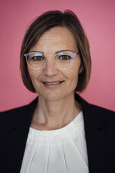 Lächelnde Geschäftsfrau mit Brille vor rosa Hintergrund - JOSEF09136