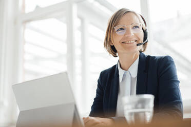 Zufriedener Anrufer mit Headset, der mit einem Tablet-PC im Büro sitzt - JOSEF09156