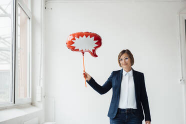 Lächelnde Geschäftsfrau mit Sprechblase Ballon vor der Wand im Büro - JOSEF09170