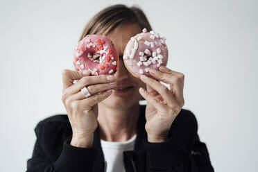 Geschäftsfrau bedeckt Augen mit Donuts vor weißem Hintergrund - JOSEF09176