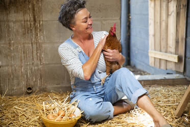 Smiling mature farmer stroking hen in chicken coop - ESTF00069