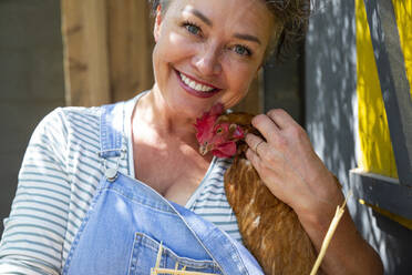 Happy mature poultry farm owner stroking with hen - ESTF00075