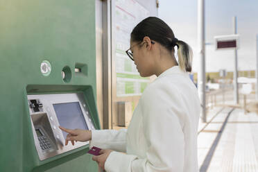 Junge Geschäftsfrau mit Kreditkarte beim Fahrkartenkauf an einer Straßenbahnhaltestelle - JCCMF06172