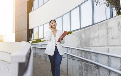 Smiling businesswoman holding file folder talking on mobile phone - JCCMF06195