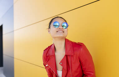 Smiling woman wearing sunglasses standing in front of yellow wall - JCCMF06205