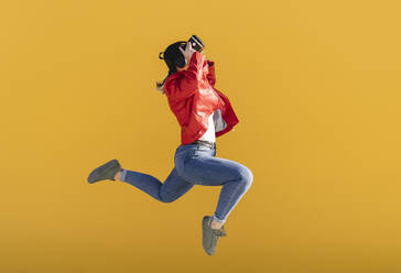 Verspielte Frau in einem Virtual-Reality-Simulator, die vor einem gelben Hintergrund springt - JCCMF06219