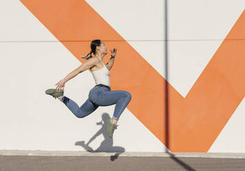 Junge Frau springt auf dem Gehweg vor einer Mauer - JCCMF06229
