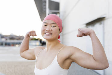 Happy woman wearing pink bandana showing biceps - JCCMF06237