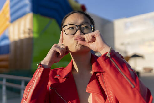 Playful woman holding lips with hand on sunny day - JCCMF06243