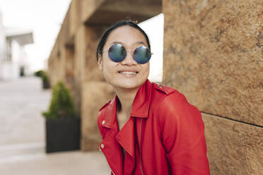 Smiling woman wearing sunglasses in front of brown wall - JCCMF06245