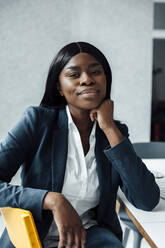 Smiling businesswoman sitting with hand on chin at desk - JOSEF09185