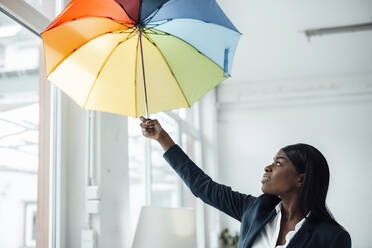 Geschäftsfrau hält bunten Regenschirm im Büro - JOSEF09228