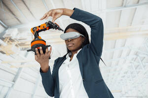 Engineer wearing virtual reality simulator holding model of robotic arm in factory - JOSEF09232