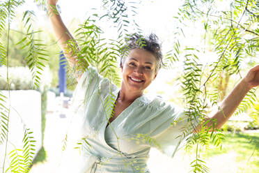 Happy woman standing with arms outstretched amidst twigs in garden - ESTF00094