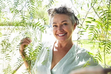 Happy woman standing amidst twigs in garden - ESTF00096
