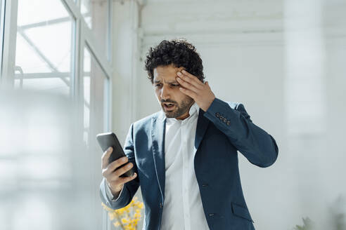 Schockierter Geschäftsmann benutzt Mobiltelefon im Büro - JOSEF09258