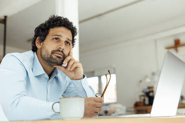 Thoughtful businessman with laptop sitting at desk - JOSEF09275