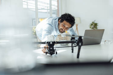 Smiling businessman analyzing drone at desk in office - JOSEF09282