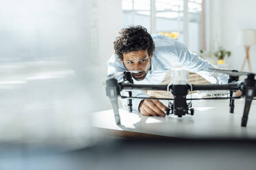 Businessman analyzing drone at desk in office - JOSEF09283