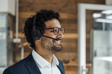 Lächelnder Geschäftsmann, der über ein drahtloses Headset im Büro spricht - JOSEF09296