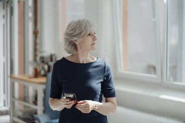 Ältere Geschäftsfrau mit grauem Haar hält Smartphone im Büro - JOSEF09317