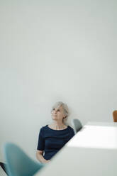 Ältere Geschäftsfrau mit grauem Haar sitzt vor einer Wand - JOSEF09335