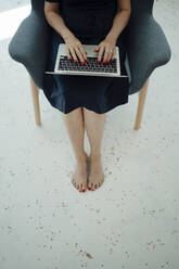 Businesswoman using laptop sitting in armchair - JOSEF09340