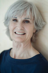 Smiling senior woman with gray hair in front of wall - JOSEF09344