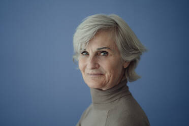 Smiling senior woman with gray hair against blue background - JOSEF09353