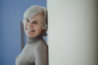 Fröhliche ältere Frau mit grauem Haar, die sich an die Wand lehnt - JOSEF09370