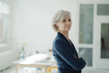 Confident senior businesswoman with arms crossed standing in office - JOSEF09387